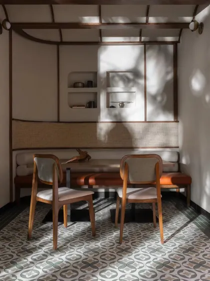 Sunlight filtering through the windows creates beautiful patterns on the patterned floor tiles of this intimate dining alcove. This cozy nook is a perfect example of our focus on creating small, private moments within a larger, bustling space.