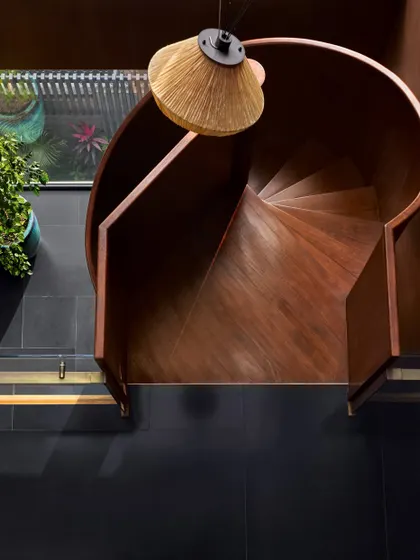 The spiral staircase at the Baid Residence, crafted from blackened steel and illuminated by a soft light from Oorjaa. The surrounding terracotta-painted walls and polished black granite floors create a symphony of textures.