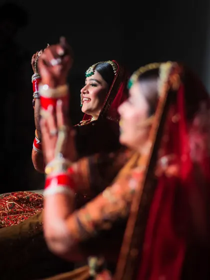 An artistic shot of the bride during the choora ceremony, seen through a reflection. This creative composition captures a traditional moment in a unique way.