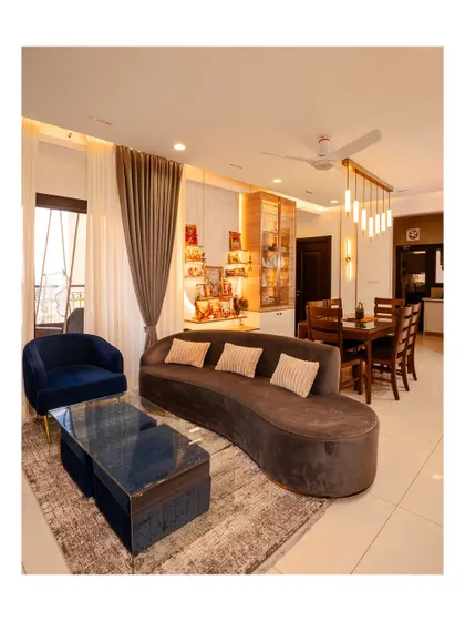 This living room features a curved dark sofa and a blue accent chair, creating a stylish contrast. The glass coffee table and elegant lighting complete the sophisticated look.