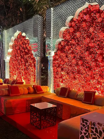 A luxurious guest seating area with a backdrop of red floral walls and silver jali panels. I create comfortable and stylish spaces for guests to relax and mingle, ensuring the decor is immersive throughout the venue.