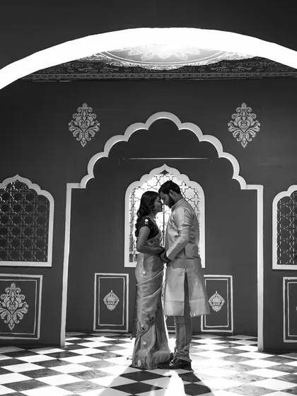 A striking black and white photograph in a room with traditional Indian motifs. The strong contrast and symmetry create a powerful and artistic pre-wedding portrait.