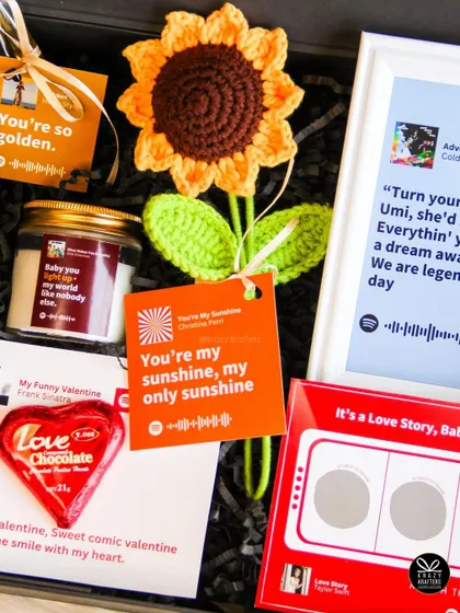 A close-up of the 'Tunes of Love' hamper, showing the crochet sunflower and personalized song tags.