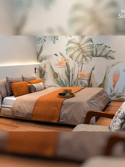 A full view of the eco-chic bedroom, where the vibrant botanical wallpaper serves as a stunning headboard. The warm orange and neutral bedding tones create a harmonious and inviting atmosphere.