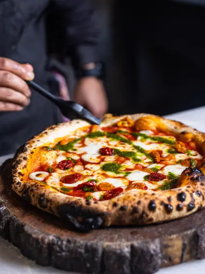A final drizzle of pesto being applied to a finished pizza. This action shot captures the final, flavorful touch before the pizza is served.