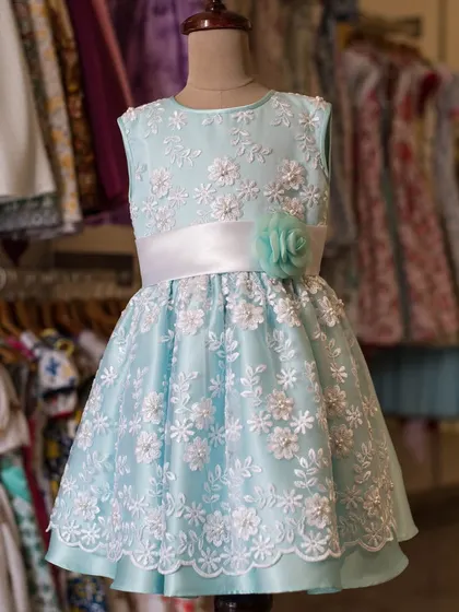 A vision in soft blue lace. This dress is perfect for parties, with its intricate floral lace overlay, a simple satin sash, and a full skirt that creates a beautiful silhouette.