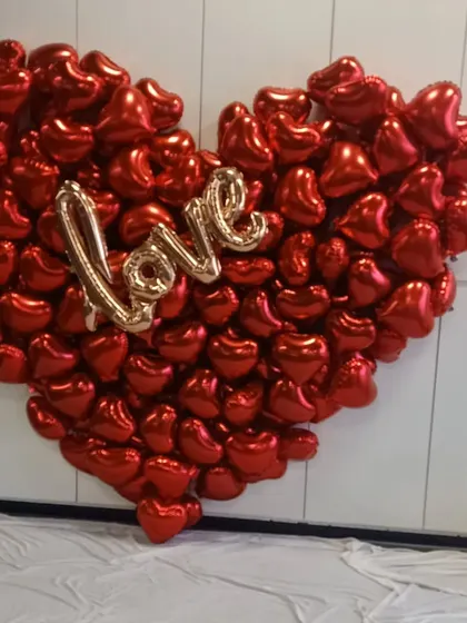 A spectacular heart-shaped backdrop made entirely of red foil balloons with a "Love" sign in the center. This is a high-impact decoration for anniversaries or Valentine's Day.