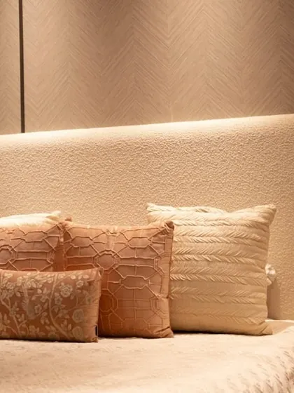 A close-up of the custom wingback headboard and layered pastel pillows in a guest bedroom. The textured fabric of the headboard adds a tactile quality to the design.