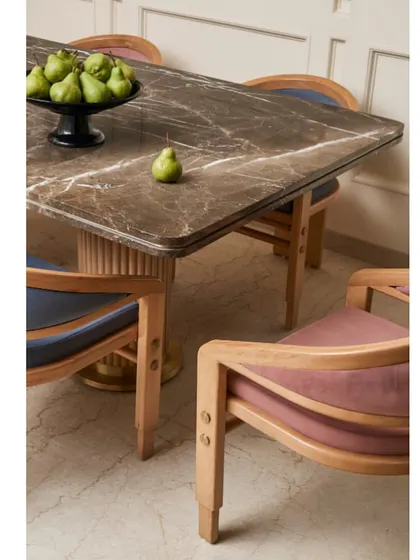 The dining space in "Virali Villa" is subtle yet impactful. The bespoke dining table features a fluted base and a dark marble top, paired with custom chairs upholstered in contrasting shades of blue and pink.