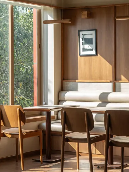 Seating nooks at QBF Coffee, where I used built-in banquettes and travertine wall panels to create comfortable, intimate zones. The large windows connect these serene interiors with the greenery outside.
