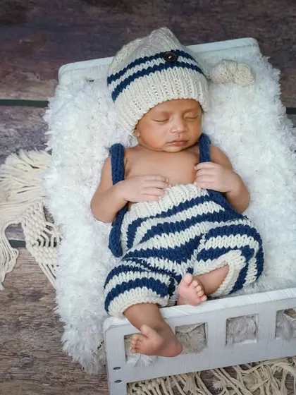 A cozy nap in a knitted outfit. The simple, rustic background and props keep the focus on the adorable, sleeping baby.