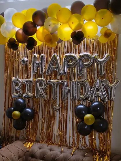 This is another shimmer curtain backdrop, this time with silver "Happy Birthday" foil letters. The balloon garland uses a mix of gold, brown, and black balloons for a stylish and modern look.