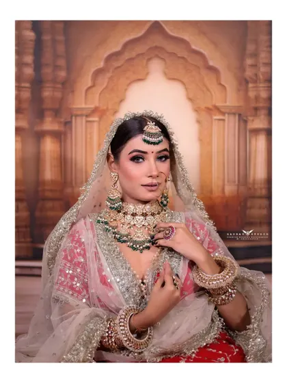 A beautiful seated portrait of the bride. Her pose is elegant and her expression is confident, perfectly showcasing her stunning red lehenga and silver-green jewellery.