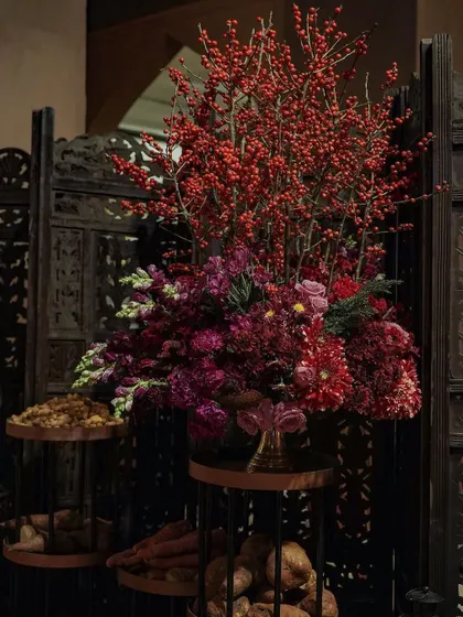 A large floral arrangement featuring red berries and deep purple blooms, set against a carved wooden screen. This dramatic piece served as a stunning focal point within the spice market section.
