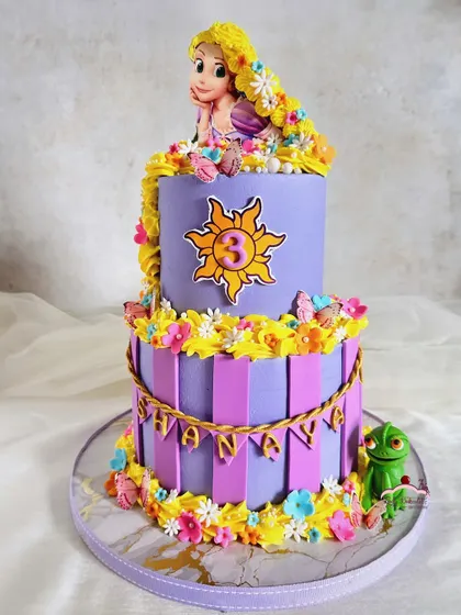 Best day ever! A Rapunzel-themed cake with her signature purple and yellow colors, a sun emblem, and a cascade of buttercream flowers in her long, golden hair.