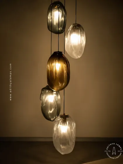 This cascading installation features pendants made of organic, free-form glass in smoked and amber tones. The textured, irregular shapes create a beautiful, water-like effect, perfect for adding a sense of calm and artistry to a room.