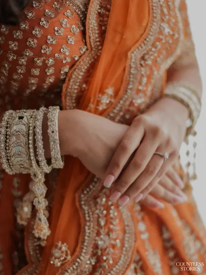 The beauty is in the details. This shot focuses on the bride's hands, adorned with intricate bangles and her wedding ring, resting on the rich fabric of her orange lehenga. It’s these small details that complete the story.
