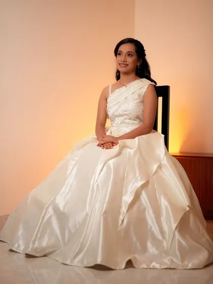 A full-length portrait of our bride seated, showcasing the beautiful volume and sheen of her custom-made satin wedding gown.