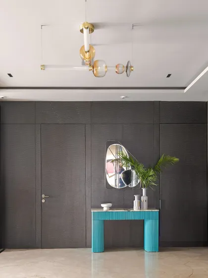 A stylish foyer featuring a dark, textured wall with hidden doors. A bright turquoise console table provides a beautiful pop of color and contrast, showcasing our bold design choices.