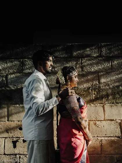 A dramatic portrait using light and shadow. The couple stands against a brick wall, the play of sunlight creating a moody and artistic feel that highlights their connection.