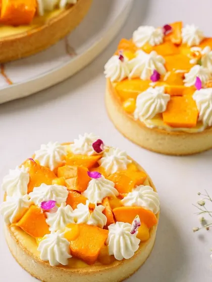 Individual mango tarts, styled with whipped cream and flowers. This shot is perfect for showcasing delicate pastries and highlighting fine craftsmanship.