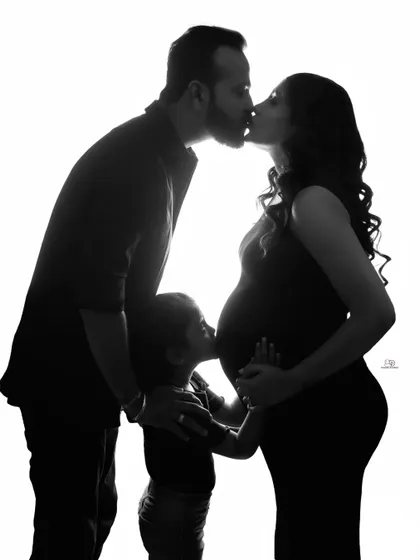 A powerful and artistic silhouette of a family's love. The dad kisses the mom, while their child kisses the baby bump, creating a beautiful and symbolic image of their growing bond.