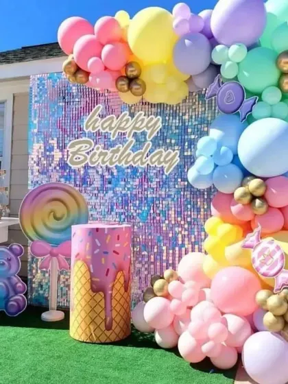 A sweet candy-themed birthday party with a colorful shimmer wall and a pastel balloon arch in an outdoor setting.