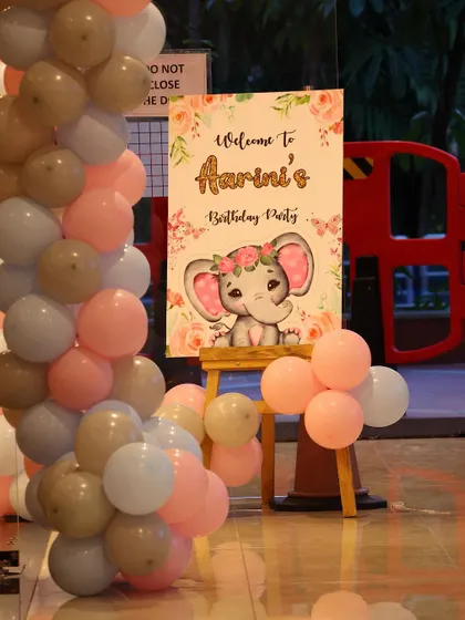 A cute elephant-themed welcome board for a birthday party. The sign is framed by pastel-colored balloons, creating a sweet and inviting entrance.