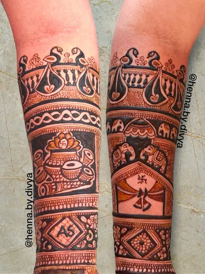 A close-up of the start of a bridal mehendi on the forearms. This design features auspicious symbols like the kalash and swastika, along with peacock and elephant motifs.
