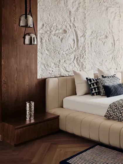 A detail shot of the master bed, showing the channel-tufted base and the contrast between the textured white wall and the warm wood paneling. Pendant lights add a modern touch.