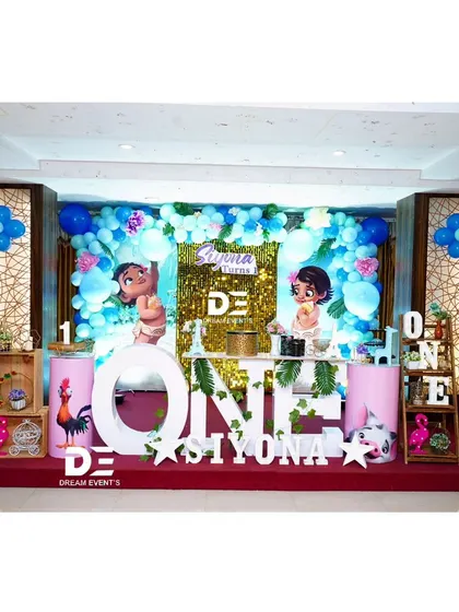 An adventurous Moana themed first birthday for Siyona. The stage includes a shimmering gold sequin backdrop, character cutouts, and large 'ONE' letters.