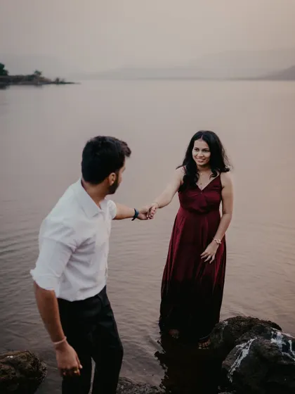 A playful moment during a lakeside pre-wedding shoot near Pune. The groom leads the bride into the water, creating a spontaneous and romantic scene against the dusky landscape.