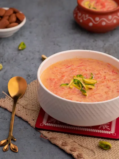A comforting bowl of Gajar Kheer, or carrot pudding. The simple, clean styling with a garnish of pistachios highlights the creamy texture and warm color of this classic Indian dessert.