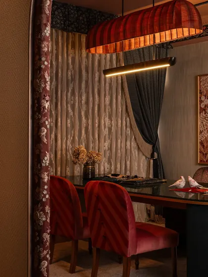 A detail of the client interaction zone, focusing on the custom red chairs and the layered drapery. The light from the bespoke chandelier catches the texture of the curtains, adding warmth and drama to the space.