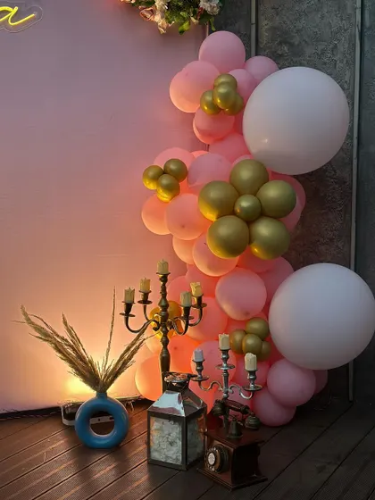 A close-up of the decor elements for Sanna's birthday, including elegant candelabras, pampas grass in a modern vase, and a warm-toned balloon garland.