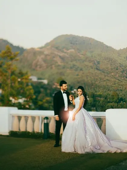 A fairytale-like portrait of a couple on a grassy lawn with mountains in the background, the bride wearing a stunning light purple ball gown.