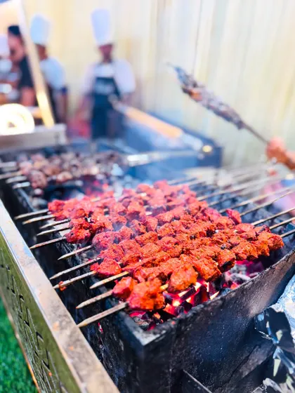 A close-up of vibrant red Khiri Kaleji kebabs cooking on skewers, showing the fresh ingredients and char from the grill.