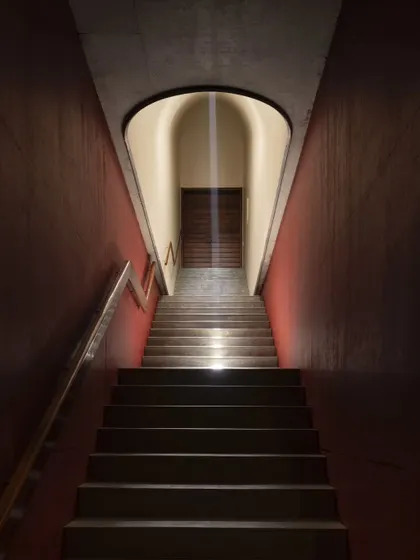 A dramatic, light-filled staircase at the Vismaya museum. A narrow slit of light from a skylight above illuminates the path, creating a powerful, almost spiritual transition between gallery levels.