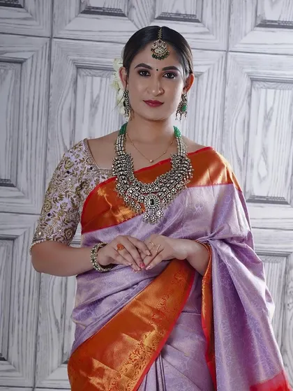 This soft lavender silk saree with a bright orange border is a unique and elegant choice for a reception or engagement. The subtle sheen of the silk is complemented by the heavy silver jewelry.