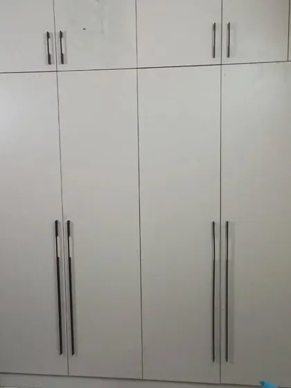 A practical and large wardrobe with white laminate and long black handles, providing a clean and functional storage solution.