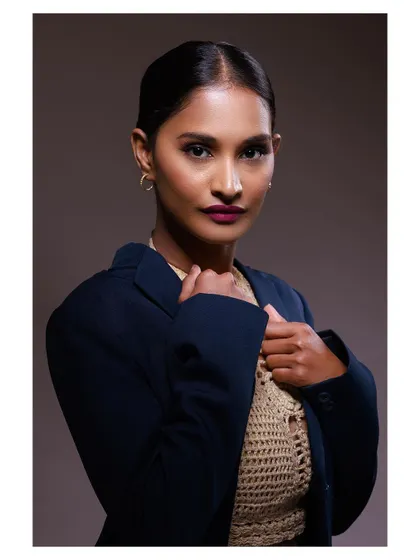 A powerful and confident portrait of a model in a blazer and crochet top. The strong lighting and direct gaze create a look of modern professionalism.