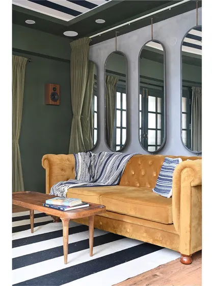 The media room features a plush, oversized mustard yellow sofa, perfect for sinking into. We hung a series of long mirrors to create a sense of depth and reflect light in the dark-toned space.
