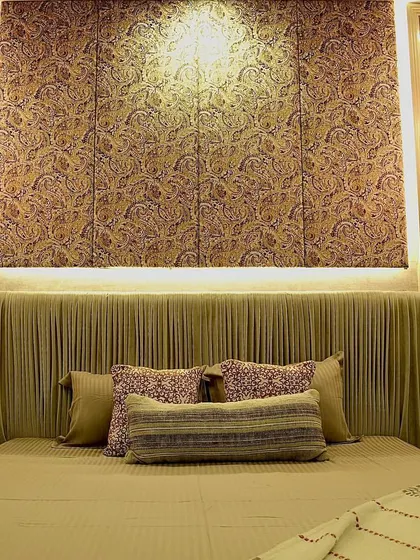 A full view of a master bedroom's feature wall, centered around our custom bed. The design includes a pleated, curved headboard, a patterned fabric wall installation, and hanging globe pendant lights for a sophisticated look.