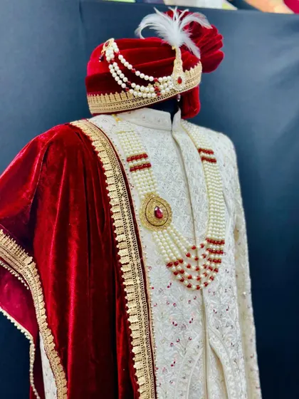 A closer look at the accessories that complete the groom's attire. The velvet turban, pearl and ruby necklace, and embroidered dupatta are all styled to perfectly match the sherwani.