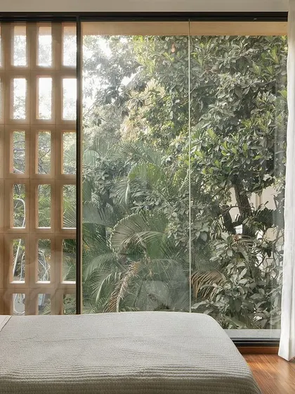 Soft morning light fills a bedroom in the Debris Block House. The jaali screen provides both natural ventilation and security, allowing the large window to be left open to the verdant views outside.