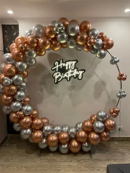 A minimalist yet chic ring backdrop for an adult birthday. The simple metal ring is accented with rose gold and silver chrome balloons, complemented by a "Happy Birthday" neon sign for a modern and understated look.