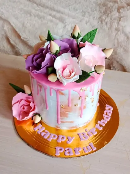 A lovely birthday cake with a pink drip effect over a brushed buttercream base, topped with a bouquet of purple and pink sugar roses.