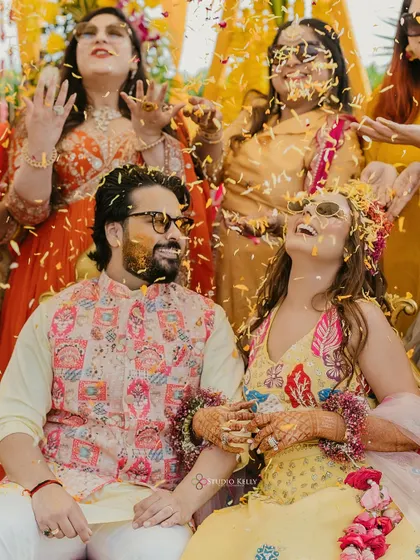 A candid shot of the couple laughing together, covered in turmeric and flower petals.