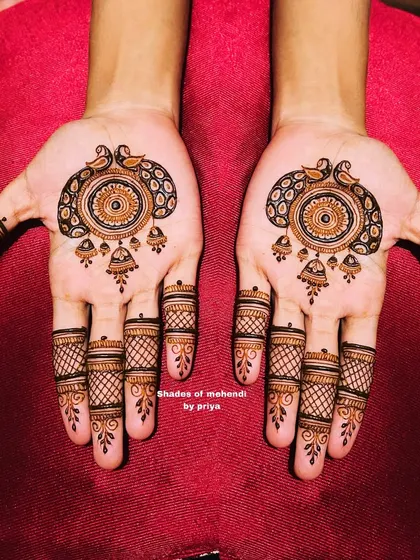 A symmetrical design featuring a mandala with peacocks and jhumkas (earrings). The fingers have a classic mesh or 'jaali' pattern.