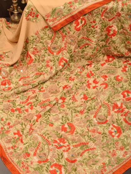 A beautiful cream-colored saree with intricate floral embroidery in shades of orange and green. This is a delicate and artistic piece.